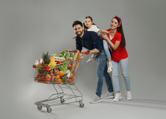 Happy family with shopping cart full of groceries on grey background © New Africa