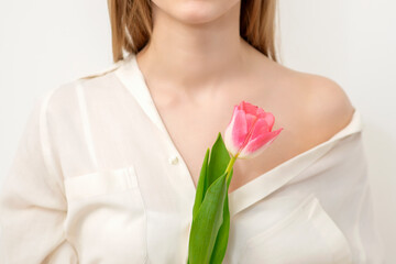 Beautiful young unrecognizable female with one tulip against a white background