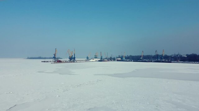 shipyard cranes view from the frozen sea. Massive blue, orange and yellow cranes in harbour. aerial drone landscape view of city port area.