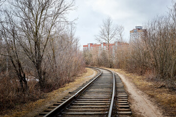 Fototapeta na wymiar A railway running to the city and large houses among bare and bald trees on an autumn or spring day
