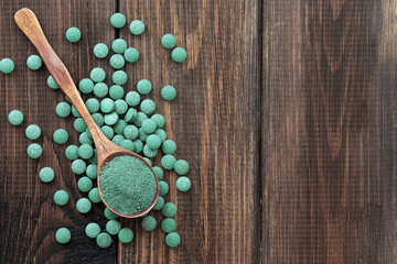 Green algae in powder and pills - chlorella, spirulina on a wooden background. Healthy green food supplement concept