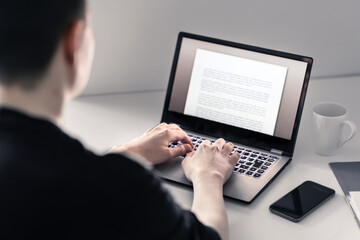 Man writing with laptop. Job applicant making his resume, cv or application. Freelance writer, journalist or teacher working in home office. Workspace with computer and phone. Blogger typing blog.