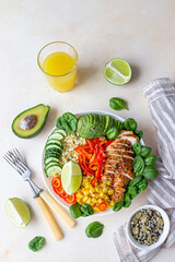 Healthy buddha bowl lunch with grilled chicken and bulgur, spinach, avocado, cucumber, bell pepper and corn on light background. Delicious balanced food concept. Top view.