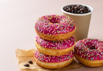 Takeaway coffee cup with coffee beans and pink glaze donuts with colorful sprinkles, pink background.