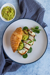 Croissant sandwich with grilled halloumi cheese, arugula and grilled zucchini, blue concrete background. Healthy breakfast or lunch. Top view.