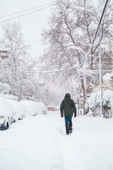 vertical view of unrecognizable traveler walking in the middle of the snow. Tourism and holidays in cold countries in christmas time. White urban scenery in december under snowstorm.