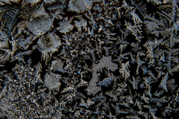 Macro of various abstract shapes of ice crystals on a glass window with black background