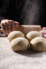 Homemade wholemeal dough for bread and female hand on wooden table with flour, rolling-pin, dark rustic background.