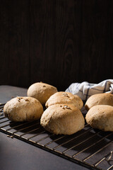 Homemade wholemeal rye wheat buns with seeds on wooden table, dark rustic background.