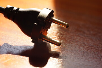 Black power plug on a brown wooden table. Side view, closeup.