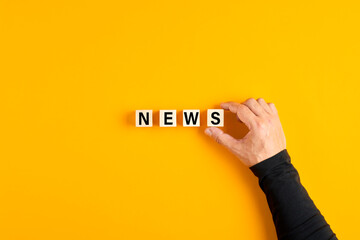 Male hand placing the wooden cubes with the word news