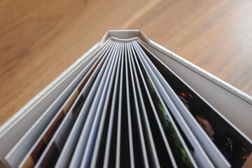 Obraz premium Opened photobook with thick plastic sheets in a hardcover on a wooden table background, Hardcover close-up. View from above. Soft focus.