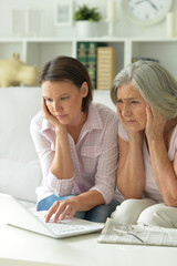 sad mother and daughter sitting at table with laptop, at home