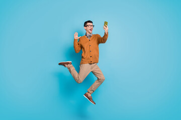 Fototapeta premium Full length photo of young excited man jump up wave hello make selfie videocall cellphone isolated over blue color background