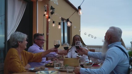 Multiracial senior friends having fun dining together and toasting with red wine on house patio dinner - Food and holidays concept - Powered by Adobe