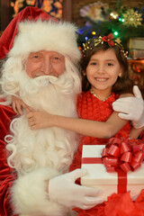 Fototapeta na wymiar Portrait of Santa Claus and happy girl with gift by Christmas tree