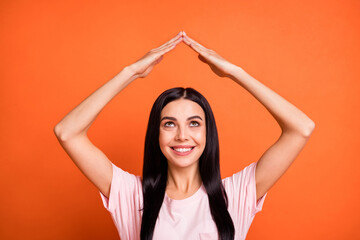 Portrait of positive lady look up arms make house figure beaming smile isolated on orange color background