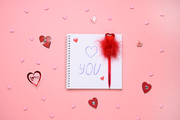 Notepad on pink background with text i love you, red pen with heart.