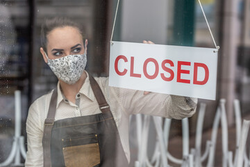 Unhappy waitress wearing face mask turns a sign closed in a bar due to coronavirus