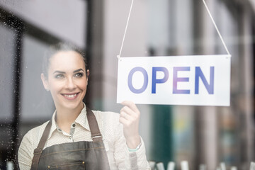 Smiling beautiful waitress turning the sign open  on a restaurant or a bar