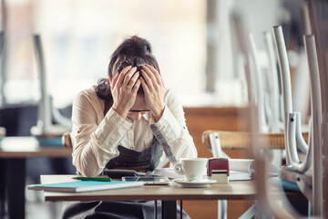 Female busines owner holds her head in hands in desperation over paperwork and tax declaration in a...