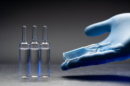 Hand in medical glove holds an ampoules with a vaccine against the coronavirus infection COVID-19. Vaccine. Ampoule with medicine. Doctor holds an injection drug in his hand.