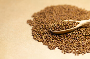 Buckwheat tea in a wooden spoon on a brown background. Buckwheat tea close-up macro photography. Scattered buckwheat tea pellets on brown background.
