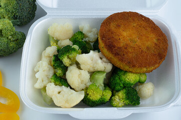 Cooked broccoli and cauliflower with vegetable burger in a white bowl.