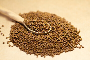 Buckwheat tea in a wooden spoon on a brown background. Buckwheat tea close-up macro photography. Scattered buckwheat tea pellets on brown background.