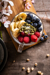 Yogurt with granola and fresh blueberries, in glass bowl over old wood background. Vintage effect.