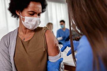 Female nurse with mask giving vaccine to patient in clinic.