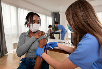 Female nurse with mask giving vaccine to patient in clinic.