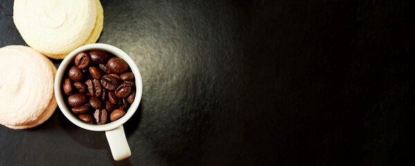 Mug with raw coffee and macaroons on the dark restaurant table. Morning snack and sweet desserts