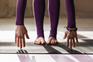 Woman in purple sportswear practicing yoga at home, performing forward bend exercise, uttanasana pose
