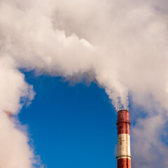 Steam comes out of the pipes of a gas thermal power plant against a blue sky