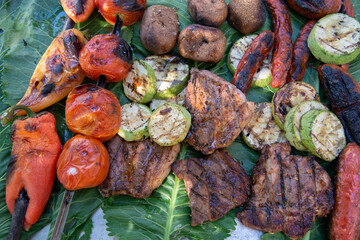 Tomatoes, zucchini, peppers, meat and barbecue sausages on a large green horseradish leaf. Grilled vegetables and meat. The concept of a summer picnic
