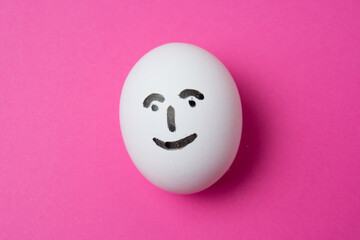 Fototapeta premium Egg with a happy face on a pink background with copy space.