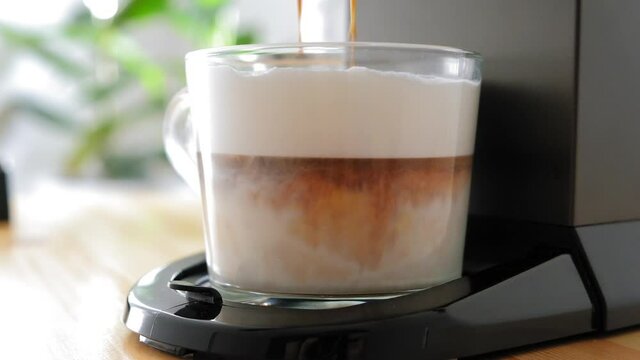 Coffee from a coffee machine is poured into a cup of milk The coffee machine makes a latte Coffee machine makes cappuccino