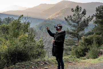 Young man using virtual reality glasses in mountains and forest. using the technology of the future in nature.
