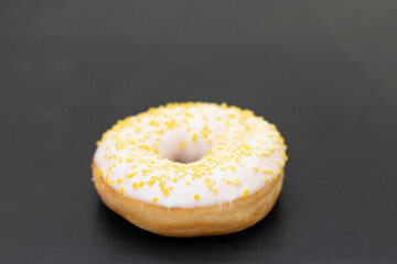 Donut with white sugar glazed and sprinkled with yellow pastry crumbs, on a black background with copy space