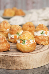 A traditional French savory choux dough cheese puff filled with fresh cheese mixed with smoked salmon in a wooden plate decoration with dill leaf. Pastry know as typically Burgundy serve as appetizer