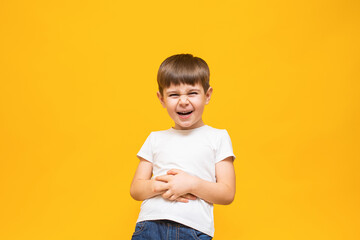 Cheerful boy laughs with his mouth wide open in a white T-shirt holding his hands on his stomach. on an isolated yellow background