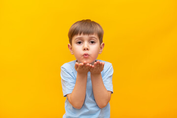Attractive little boy blowing a kiss to the camera, demonstrating love for his girlfriend or saying goodbye from a distance, isolated on yellow studio background. 