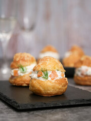 A traditional French savory choux dough cheese puff filled with fresh cheese, smoked salmon, dill leaf. Glass of champagne in background. Pastry most likely coming from burgundy serve as an appetizer 