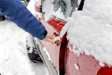 Shot of a man's arm wearing blue winter jacket opening snow covered car door. Unrecognized man...