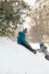 Boy in a green jacket and hat on the hill. Children play in the snow. Winter city.