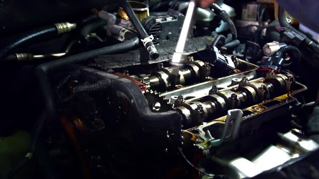 Valve cover Repair in Auto Shop Footage. A four-cylinder in-line engine under the hood of the car with the valve cover removed with traces of yellow oil during repairs in footage.