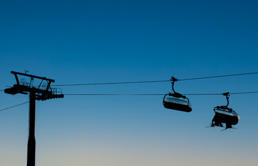 Chair ski lifts in silhouette against a clear evening sky at a winter ski sports resort.