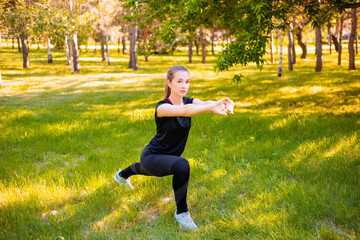 Young fitness woman doing lunges exercises to train leg muscles. An active girl does an exercise with a lunge on one leg in front. Sports activities in nature.