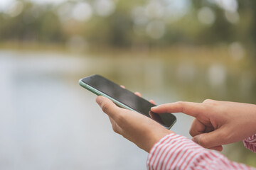 Woman hand using smart phone at outdoor nature park with sunset sky abstract background.